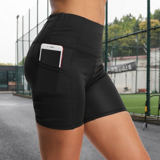 MotionMade black high-waisted compression shorts with side pocket holding a phone, worn on an outdoor sports court.