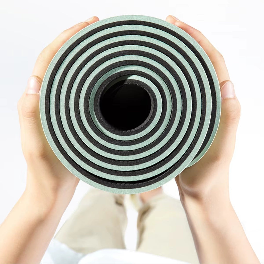 MotionMade green and black anti-slip yoga mat rolled up and held by a person for easy portability.