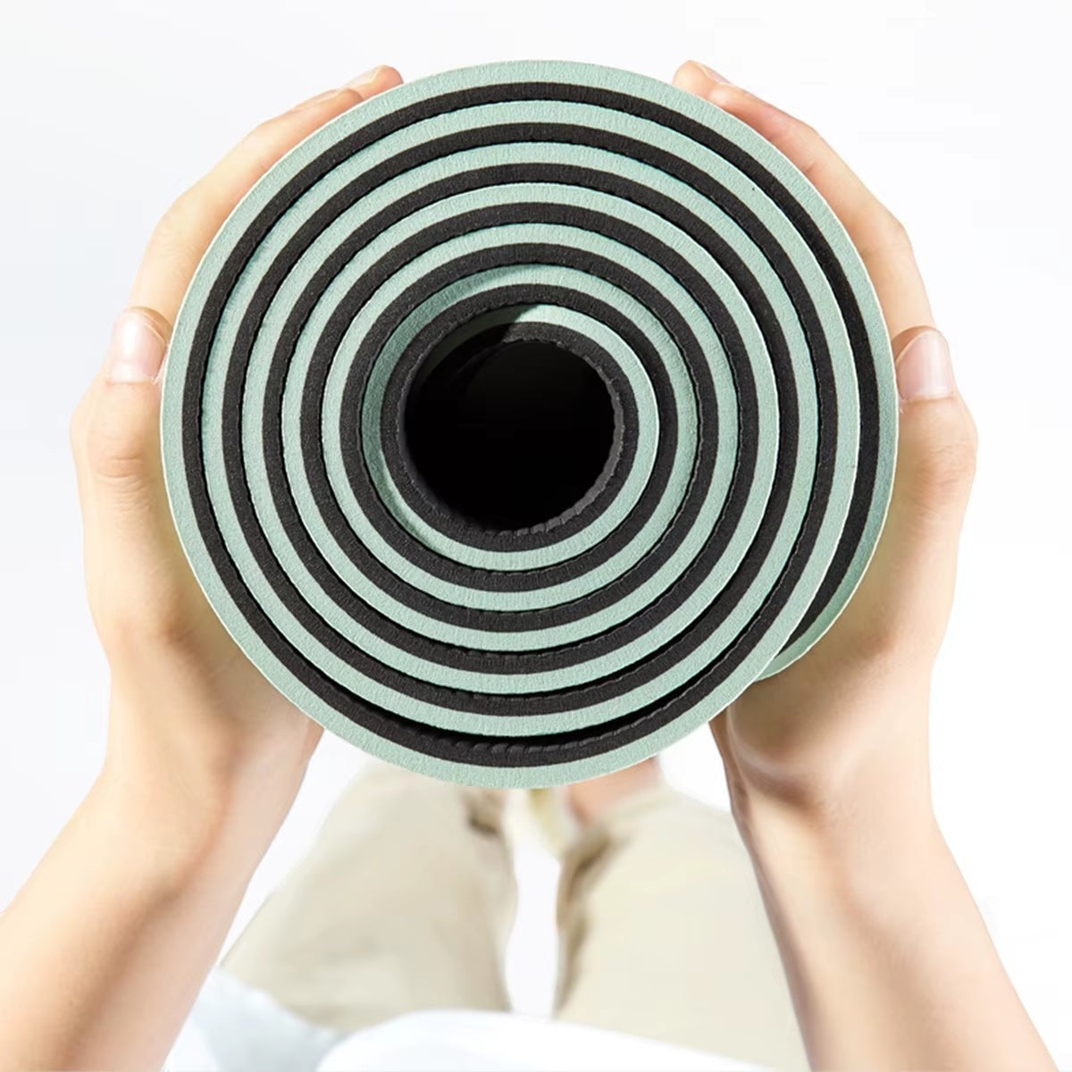 MotionMade green and black anti-slip yoga mat rolled up and held by a person for easy portability.