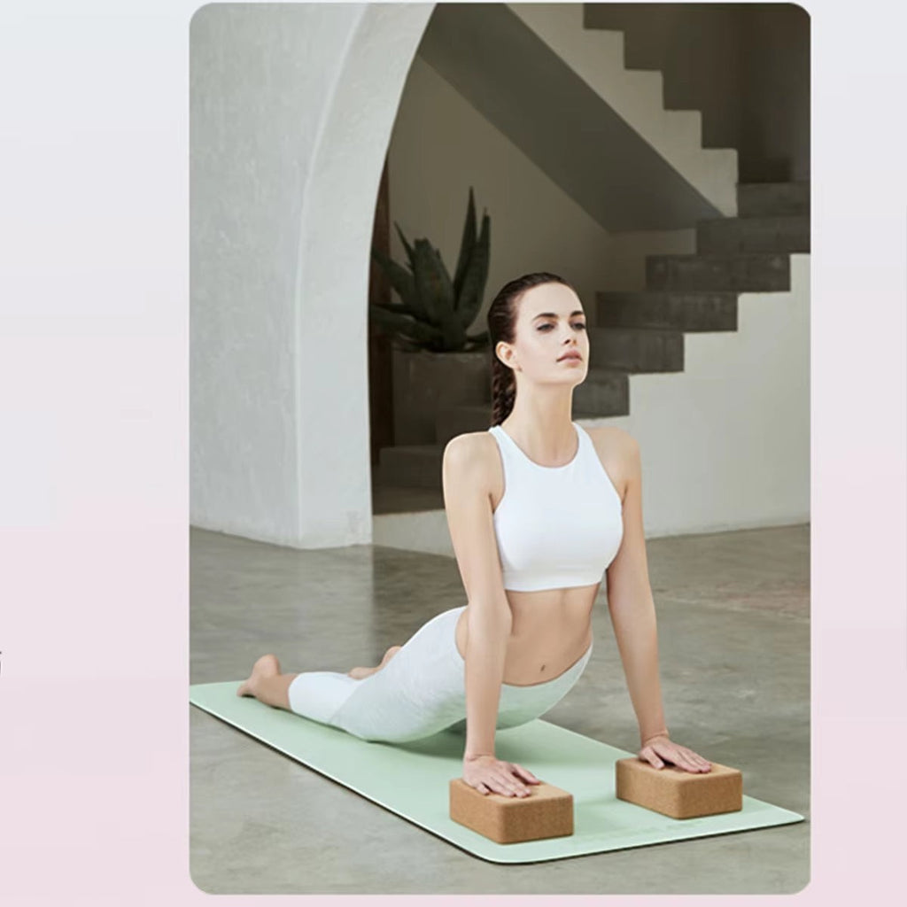 Woman in white activewear doing yoga on a green MotionMade anti-slip mat with cork blocks in a bright studio.