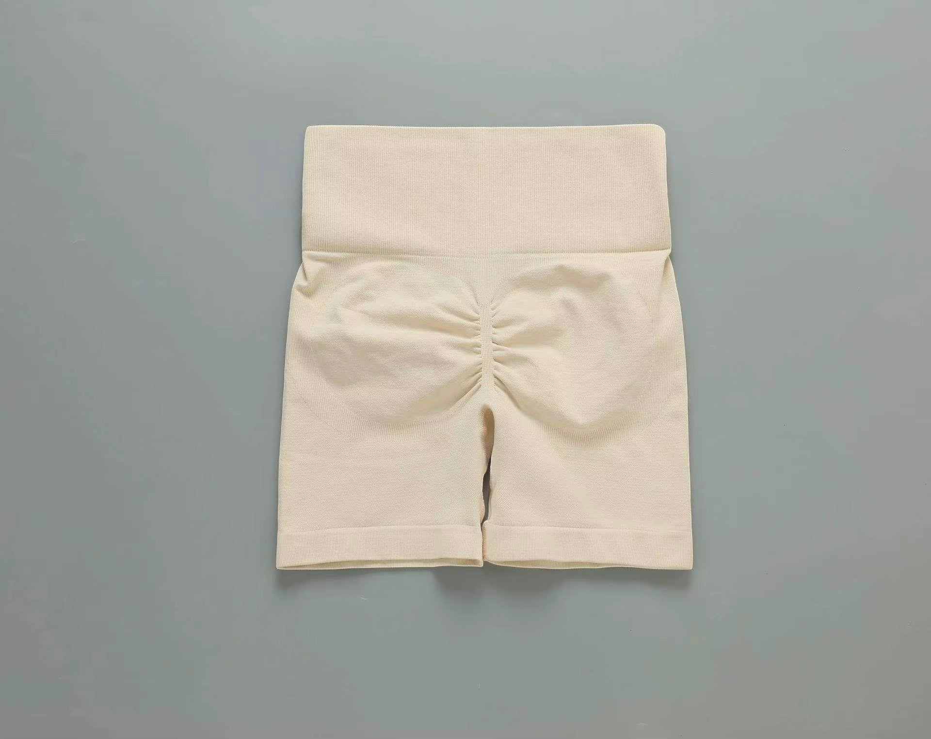 MotionMade beige high-waisted push-up workout shorts with ruched detailing for yoga and gym training.