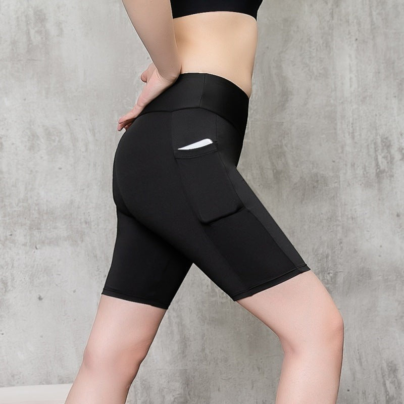 MotionMade black high-waisted compression shorts with side pockets on a model against a grey concrete background.